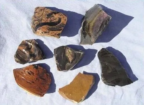 Seven pieces of Glass Buttes obsidian on a white cloth: rainbow, jet black, pumpkin, mahogany, gold sheen and double flow