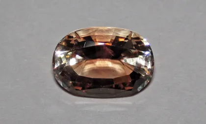 An oval faceted Oregon sunstone, pale peach to coppery brown, on a gray background